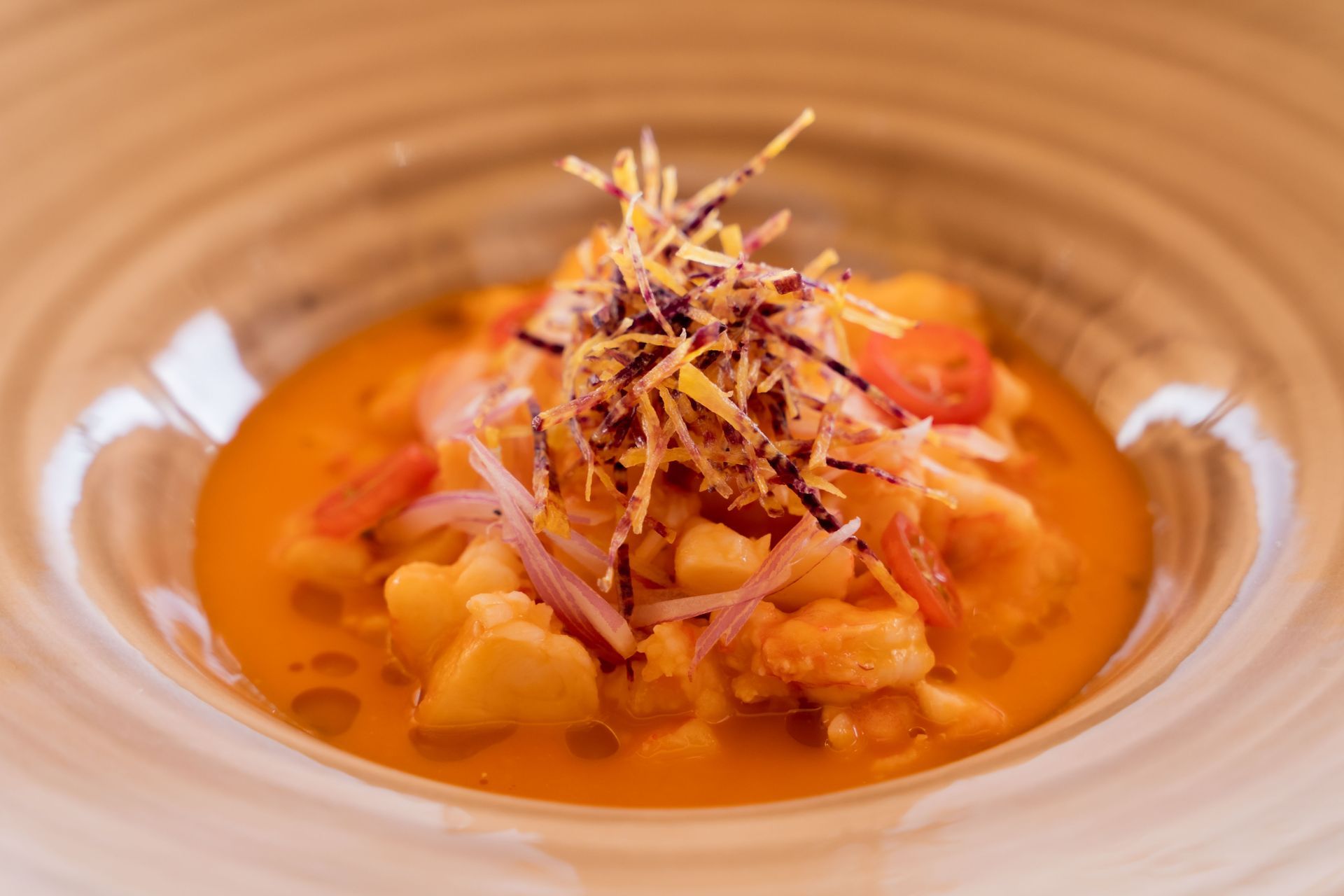 Ceviche in a bowl: diced fish in orange sauce, garnished with red onions, tomato, and crispy strands.