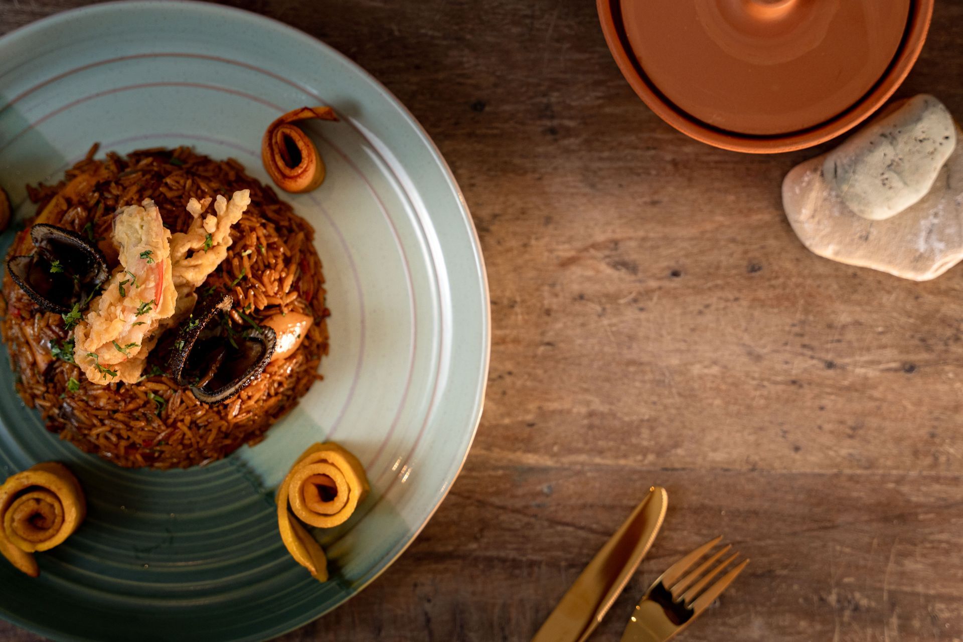 Plate of food with rice, seafood, and fried plantain spirals on a wooden table.