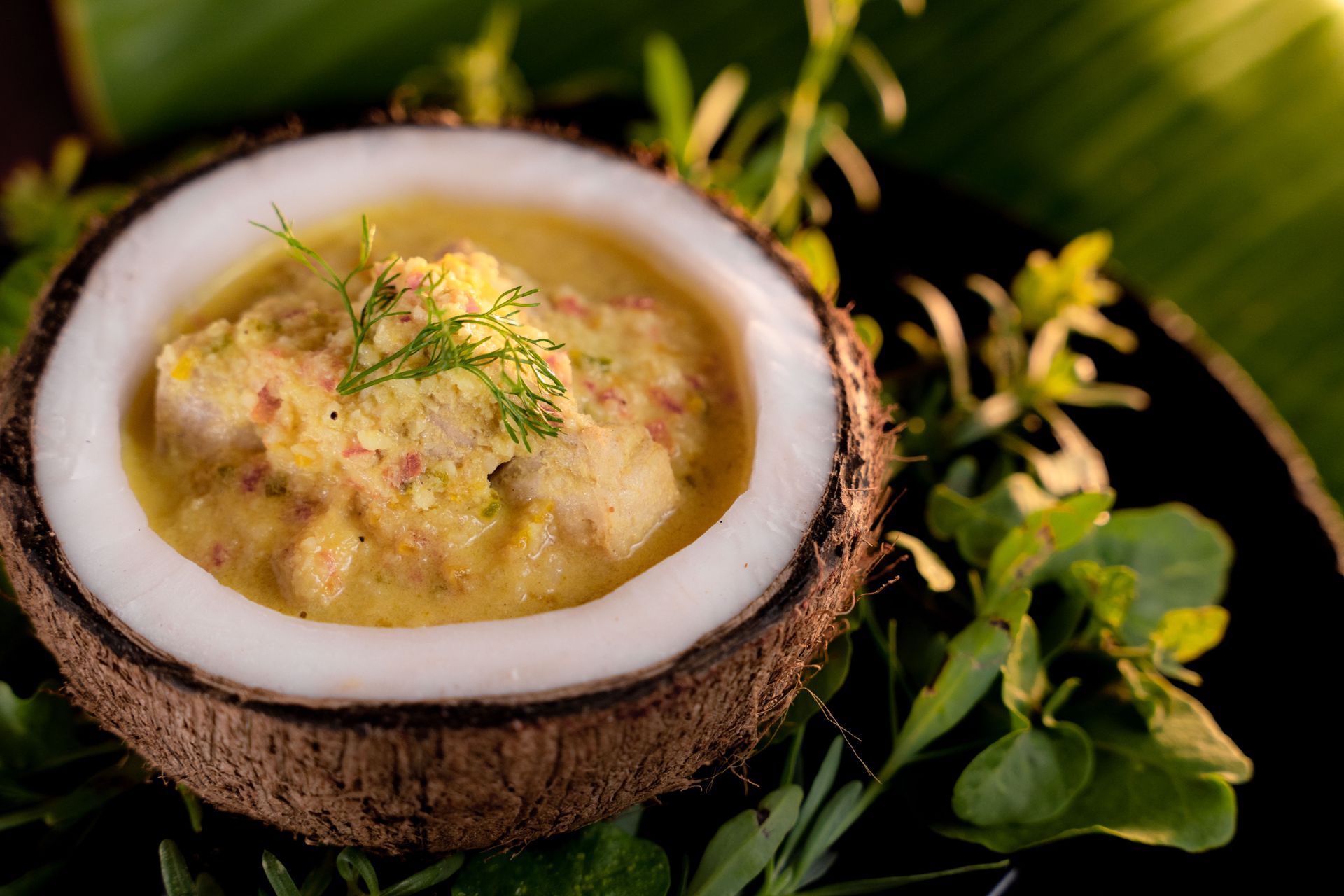 Coconut shell bowl filled with yellow curry garnished with herbs.