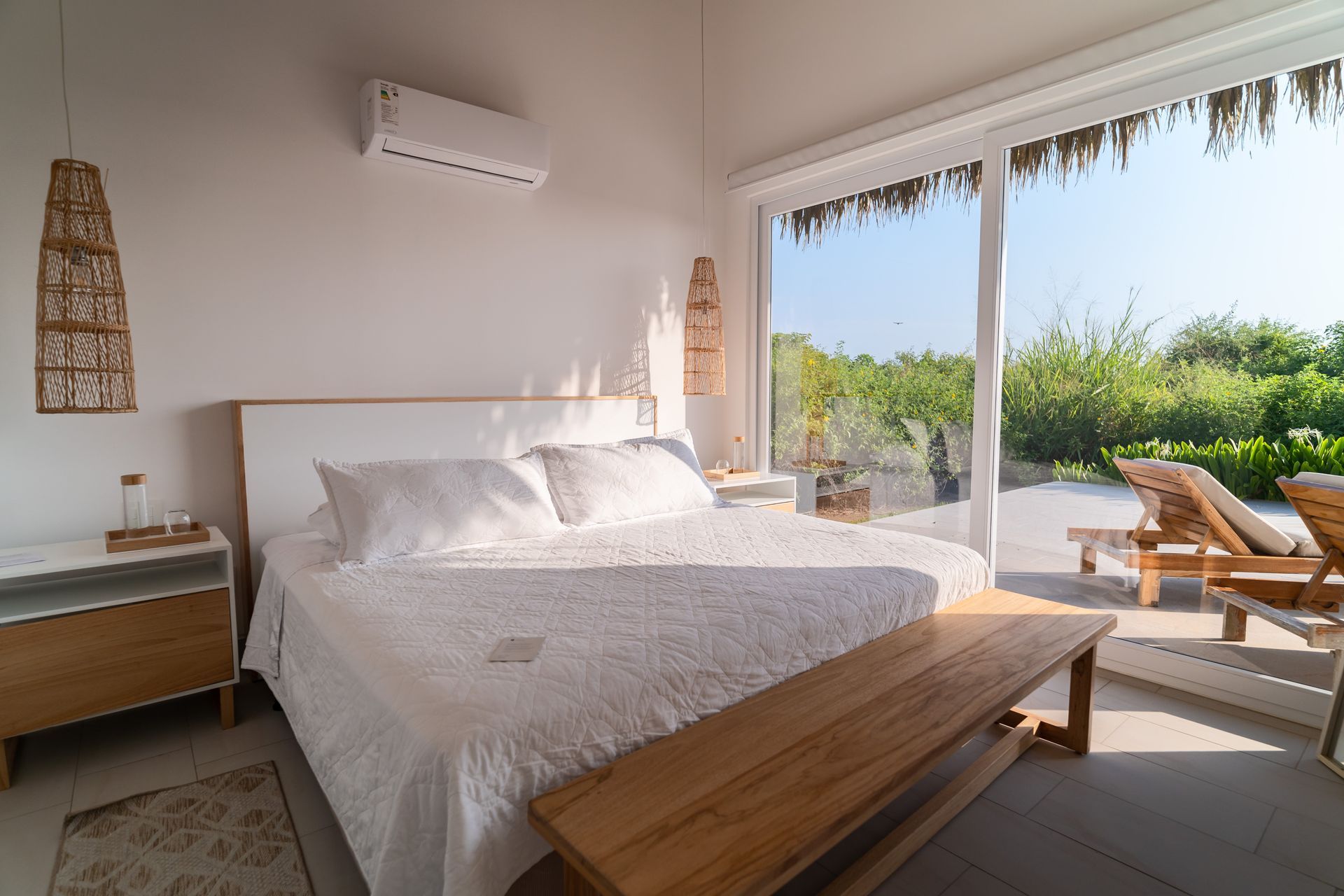 Bedroom with white bed, wooden bench, and large window overlooking greenery.