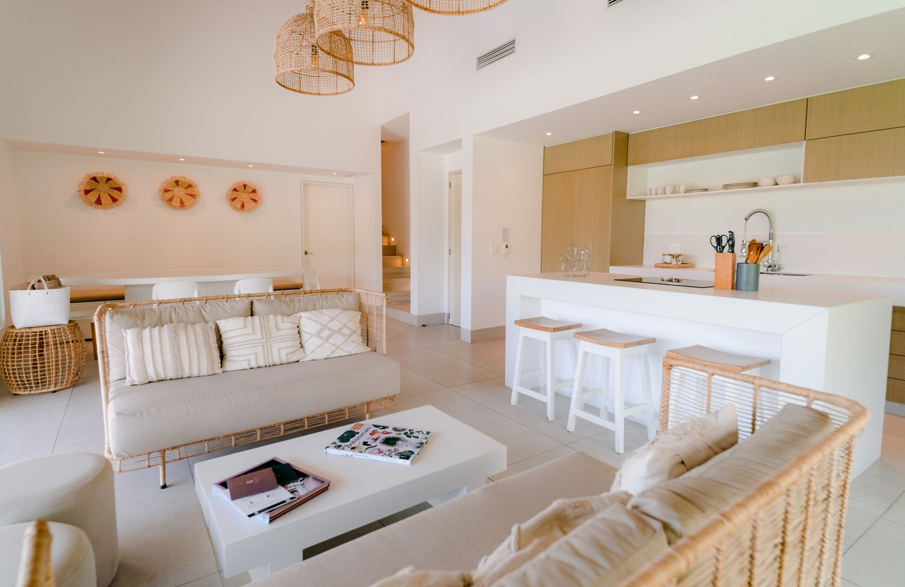 Bright living room with light-colored couches, a white kitchen island, and woven chandeliers.