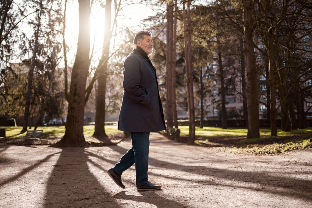 A man in a coat is walking through a park.