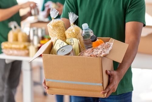 Image of man carrying box of grocery items to donate.
