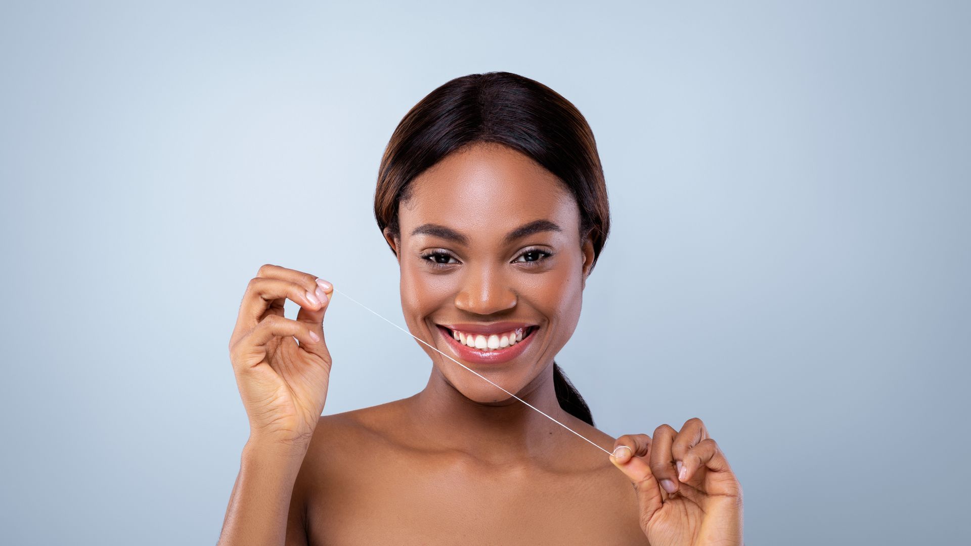 A woman with a bright smile using dental floss to maintain good oral health.