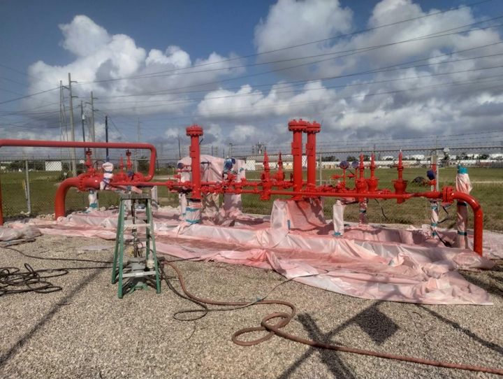 A group of people are painting red pipes in a field.