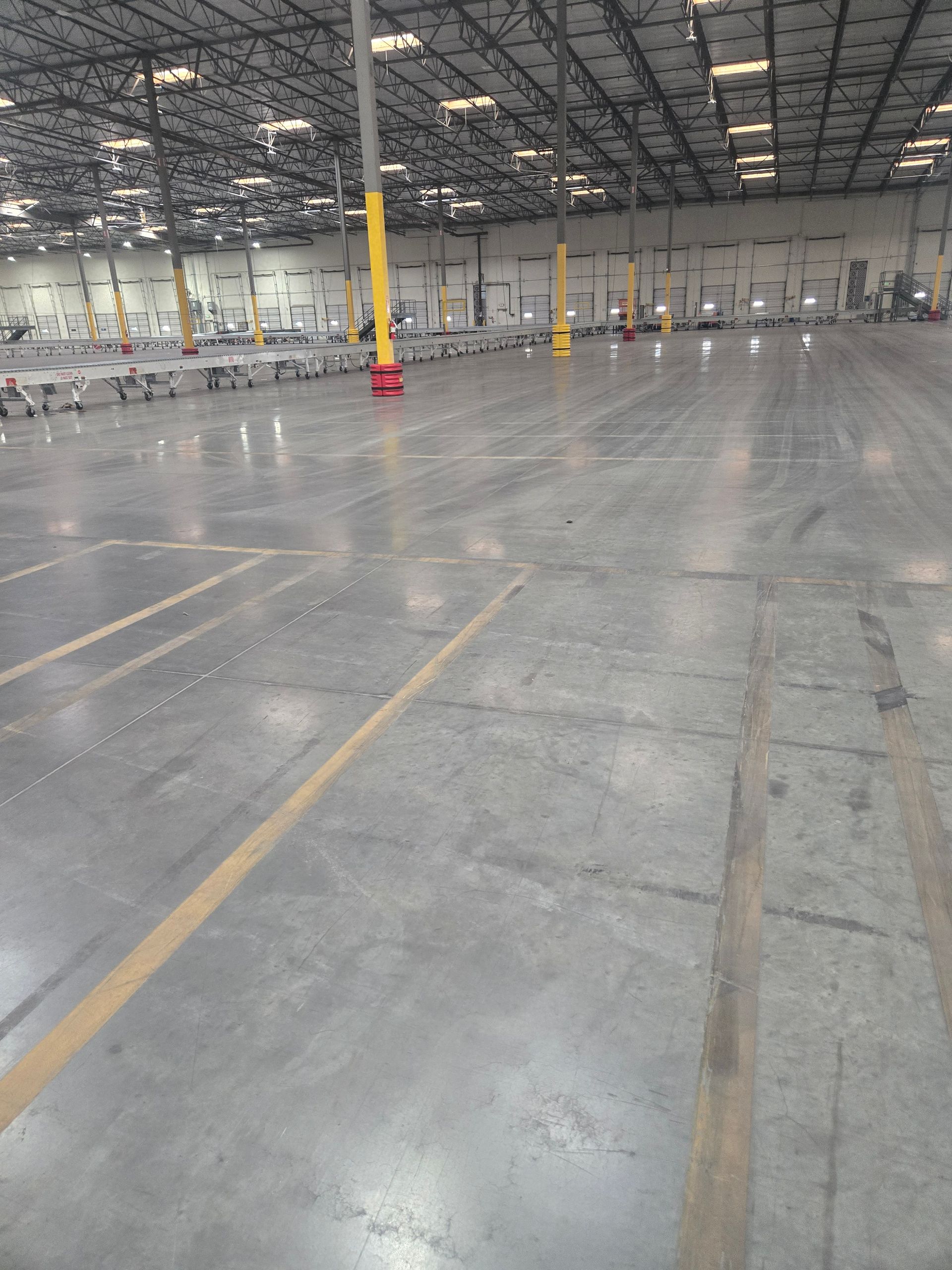 A large, empty concrete warehouse floor with yellow support pillars extending into the distance under a high ceiling.