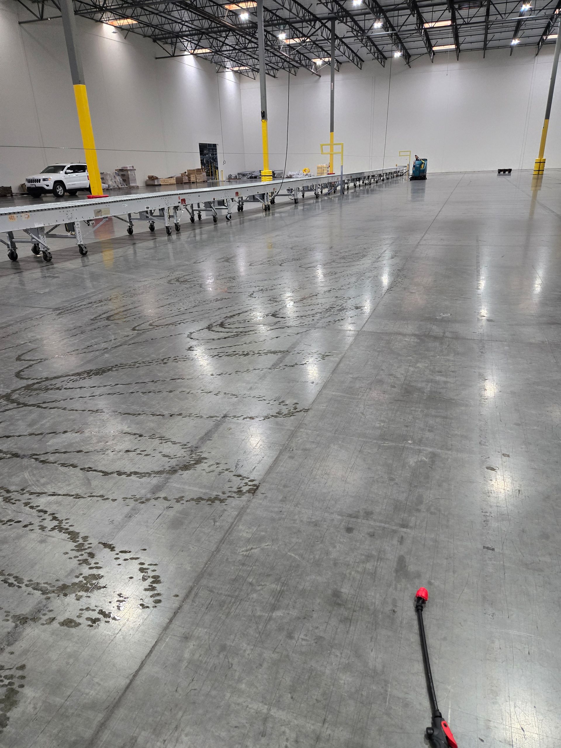 Polished concrete warehouse floor with tire tracks, long sorting conveyors, and a vehicle in the background.