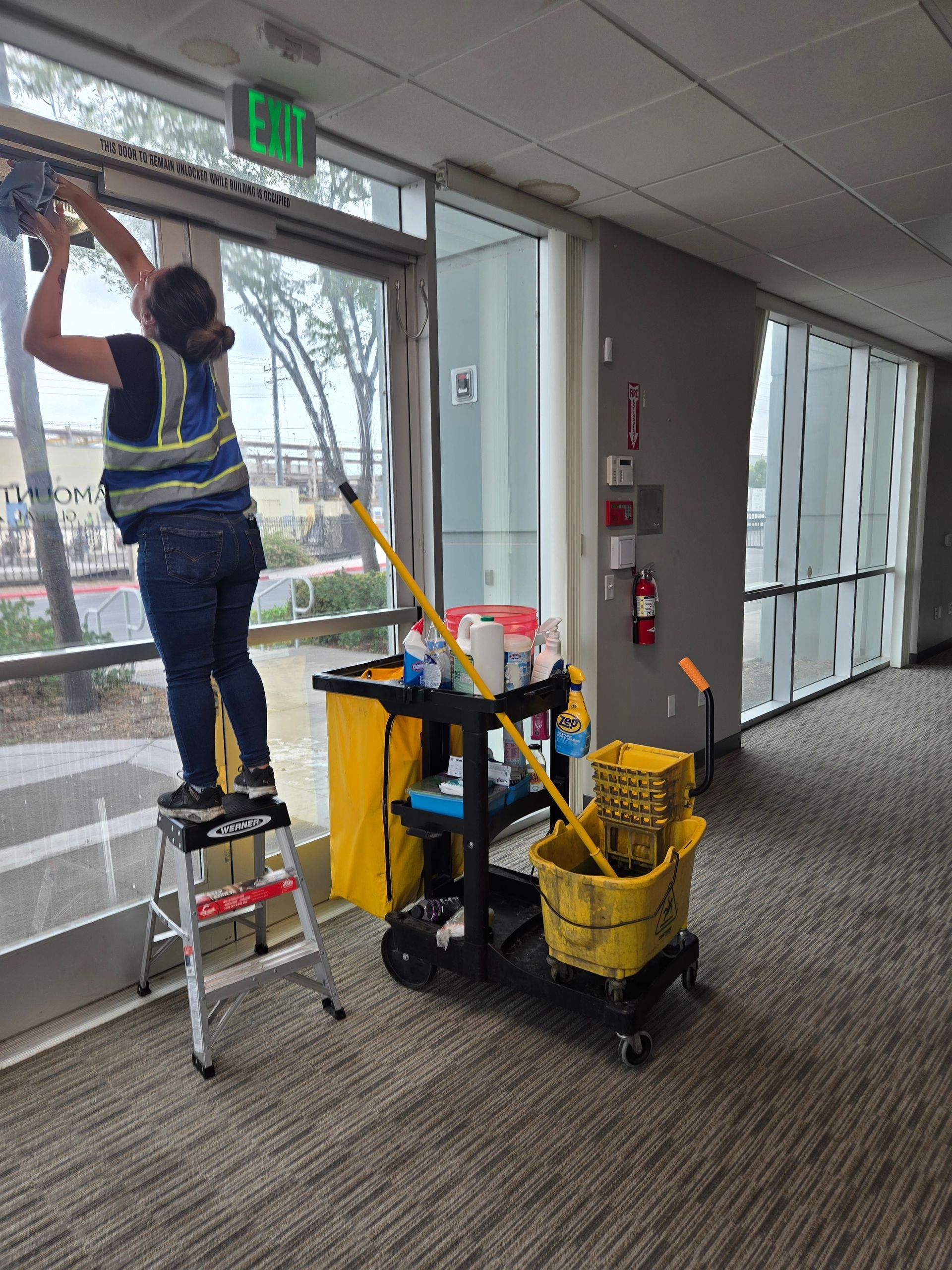 Person vacuuming a light-colored carpet in a modern living room with a gray sofa and yellow pillows.