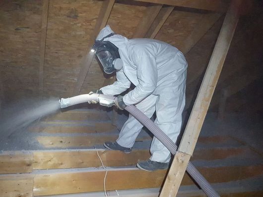 A man in a protective suit is spraying something with a hose.