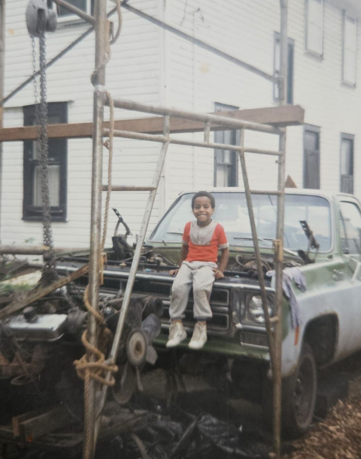 A little boy is sitting on the hood of a truck