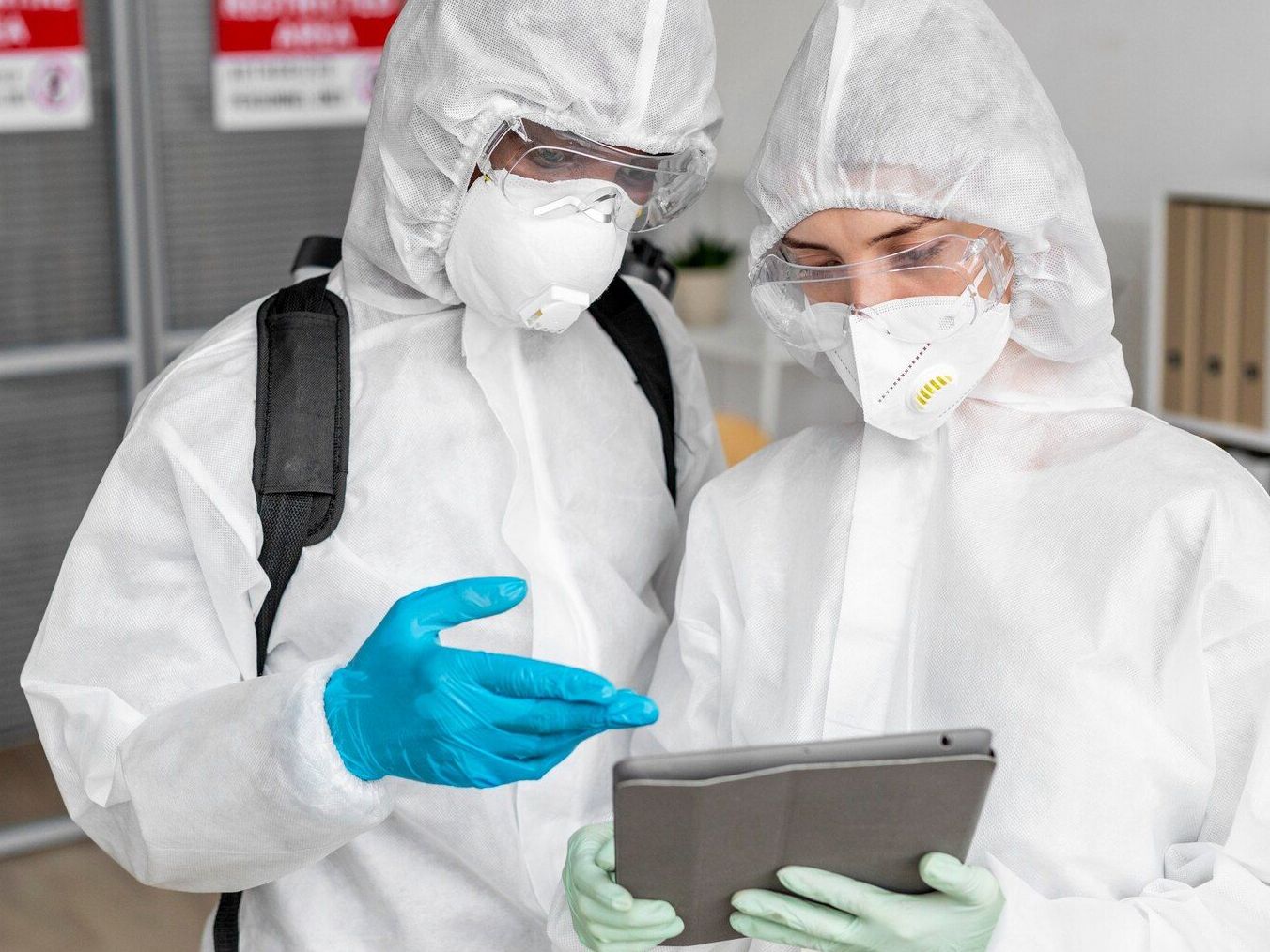 A man and a woman in protective suits are looking at a tablet.