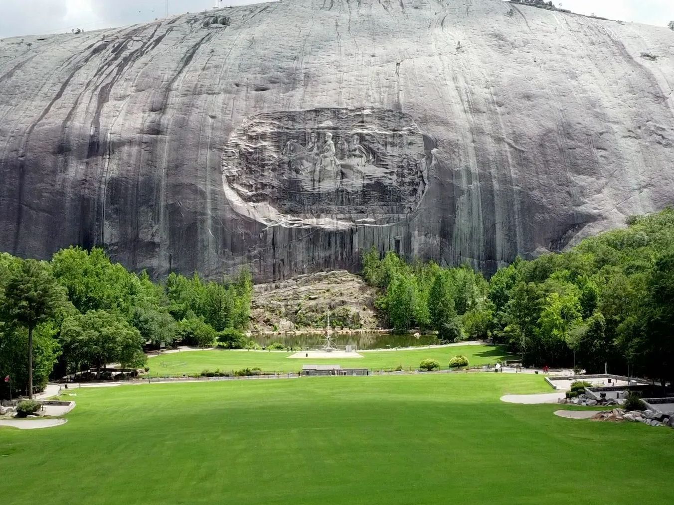 A large rock formation with a statue carved into it is surrounded by trees and grass.