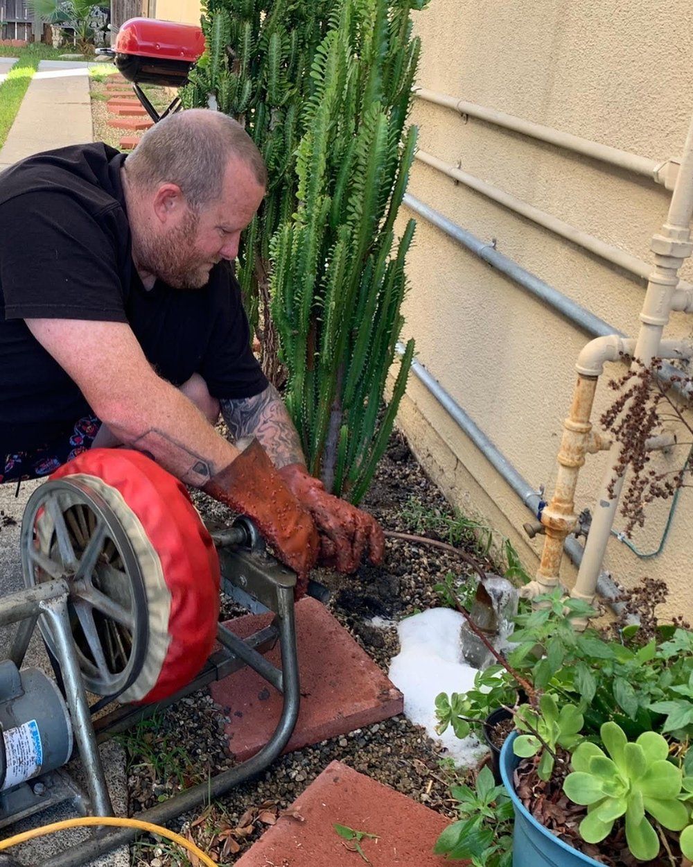 A man is using a machine to clean a drain in a garden.