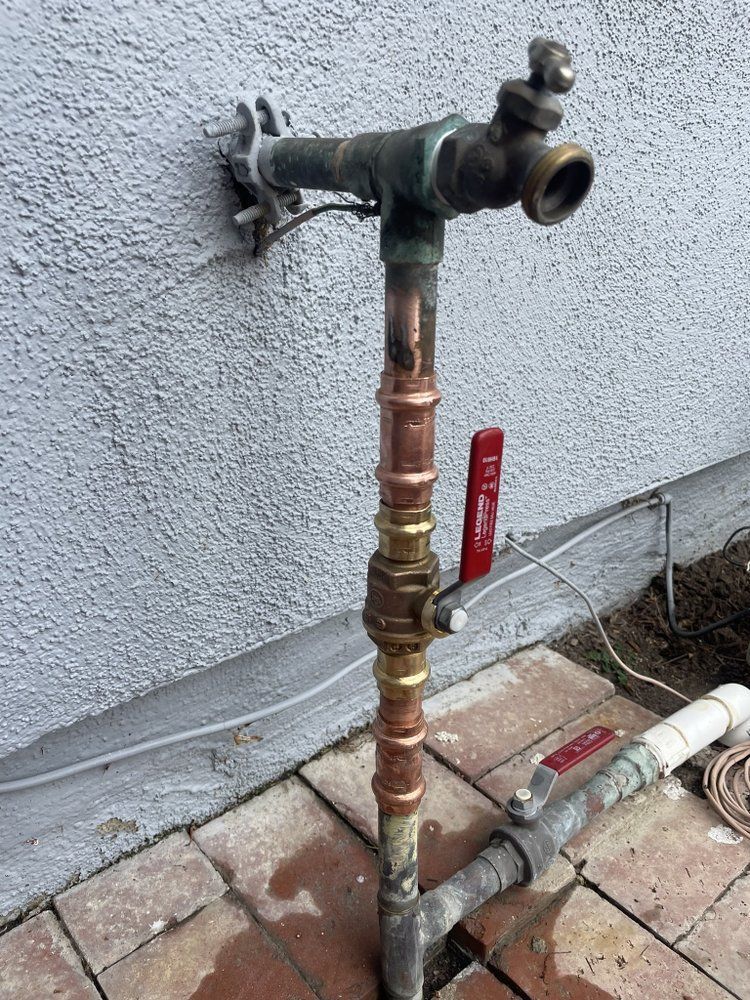 A copper pipe with a red valve is attached to a wall.