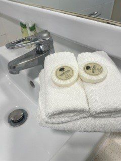 White bathroom sink with faucet, stacked white towels, two round soaps.
