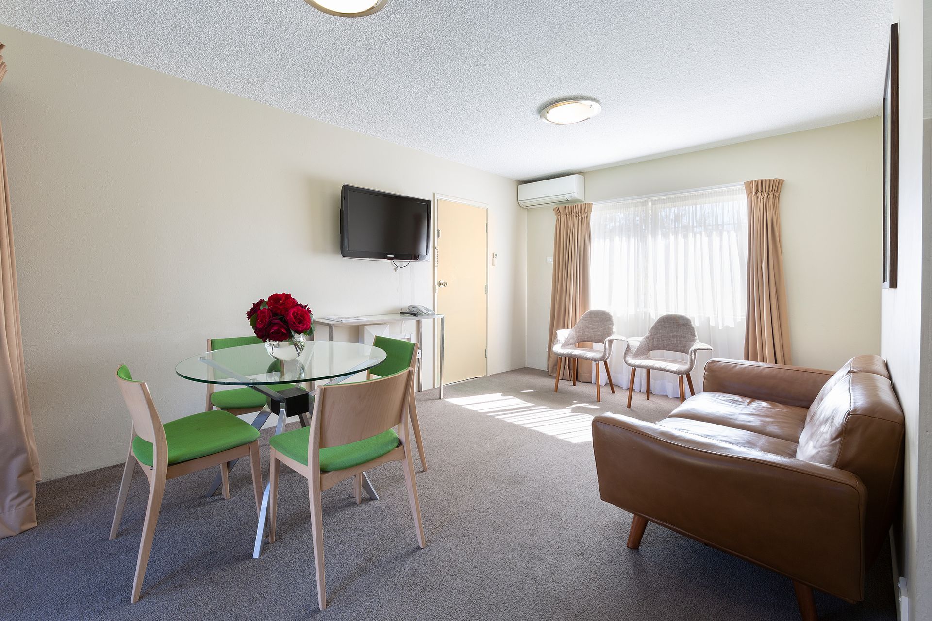 Living room with brown sofa, glass table with green chairs, and a mounted TV.