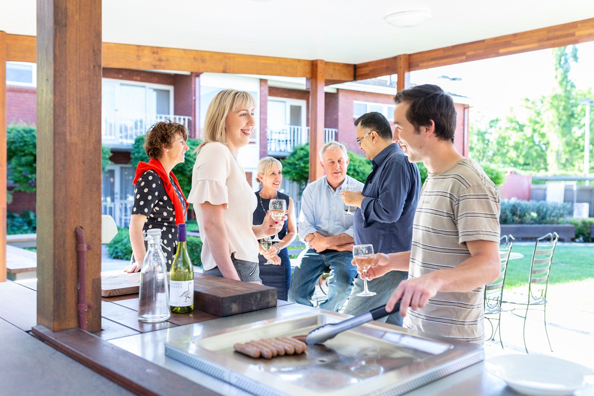 Group of people socializing, grilling food and drinking in an outdoor patio area.