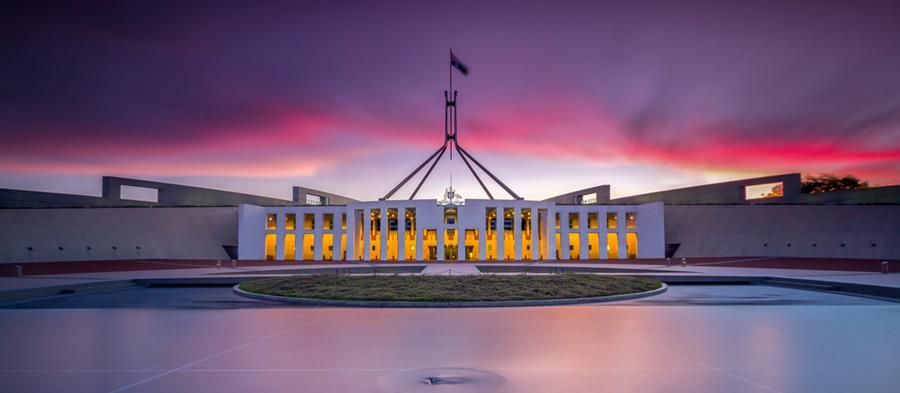 Parliament House, Canberra at dusk with a colorful sky reflected in the water.