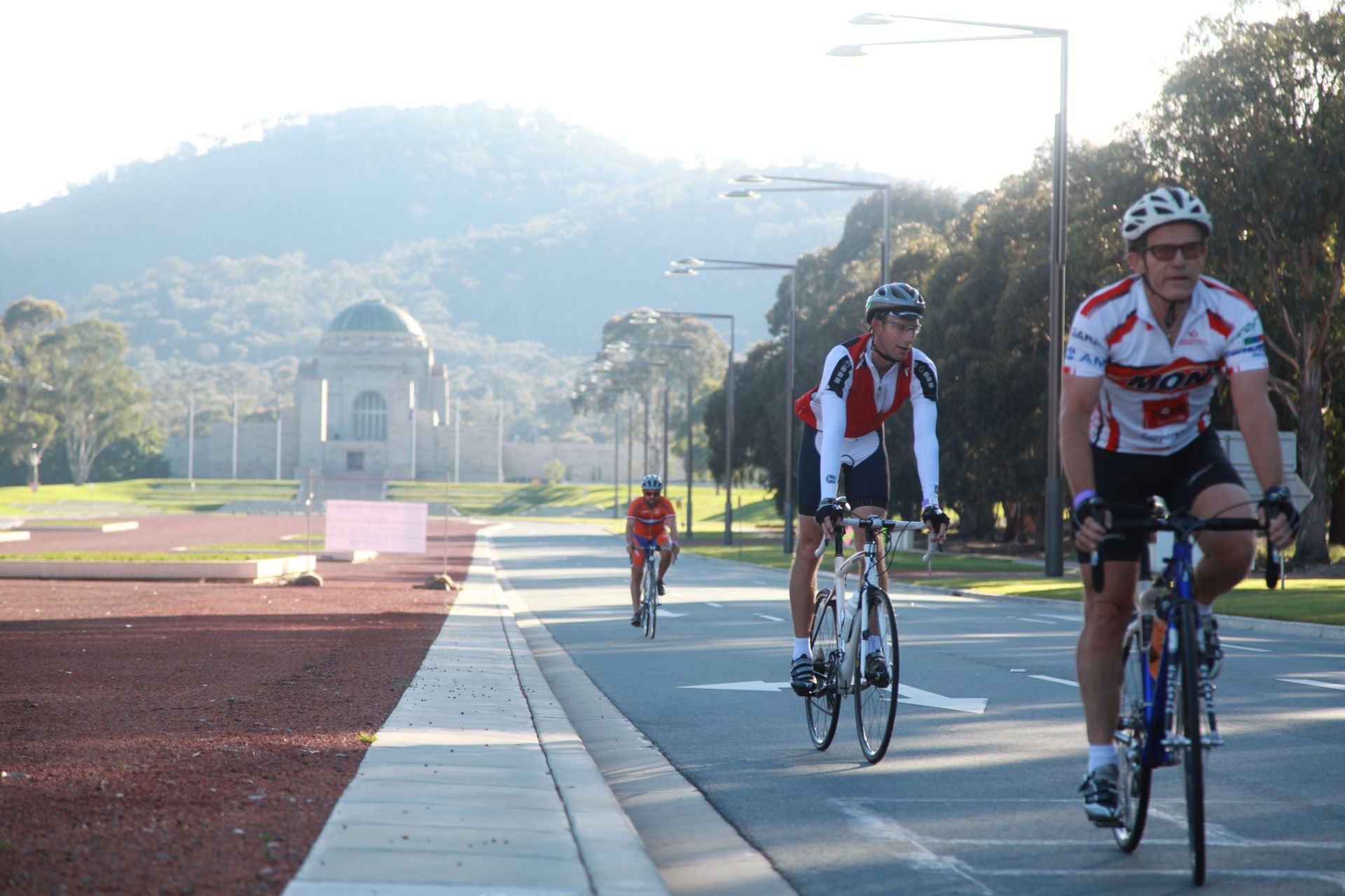 Cyclists ride along a road with a monument and mountain in the background. Sunny day.