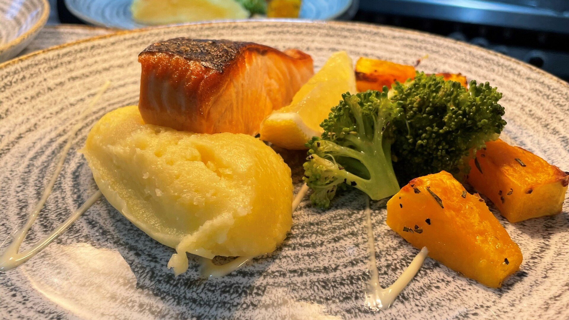 Salmon fillet with mashed potato, broccoli, roasted vegetables, and lemon on a plate.