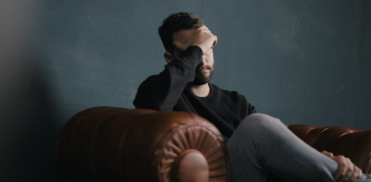 A man is sitting on a couch with his head in his hands.