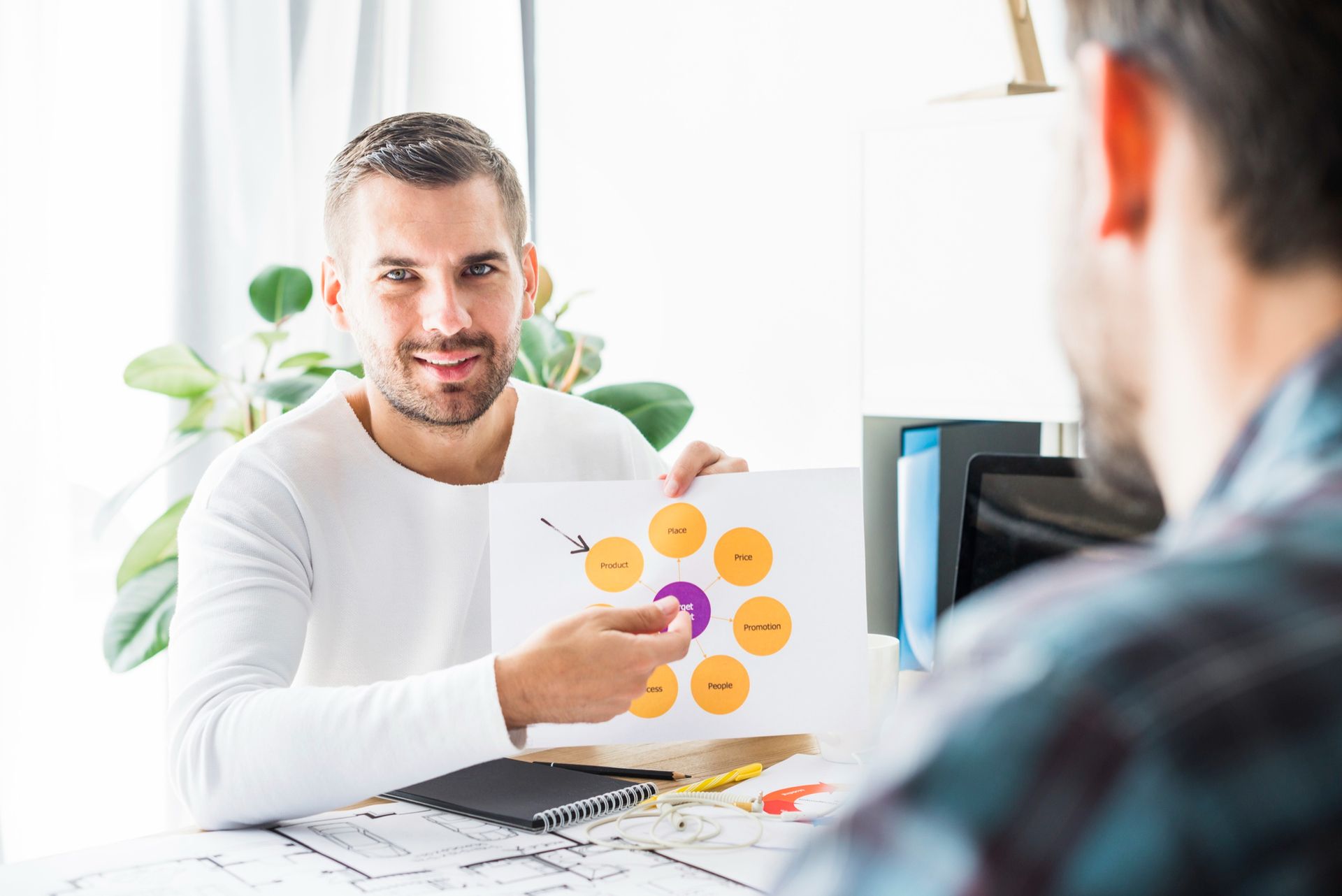 A man is sitting at a table holding a piece of paper with circles on it.