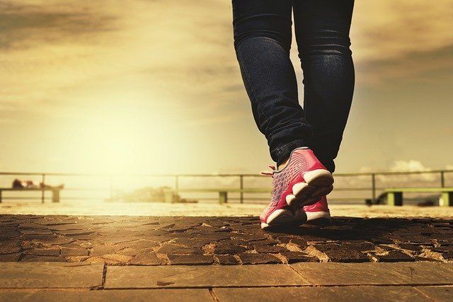 A person wearing pink sneakers is walking on a brick sidewalk.