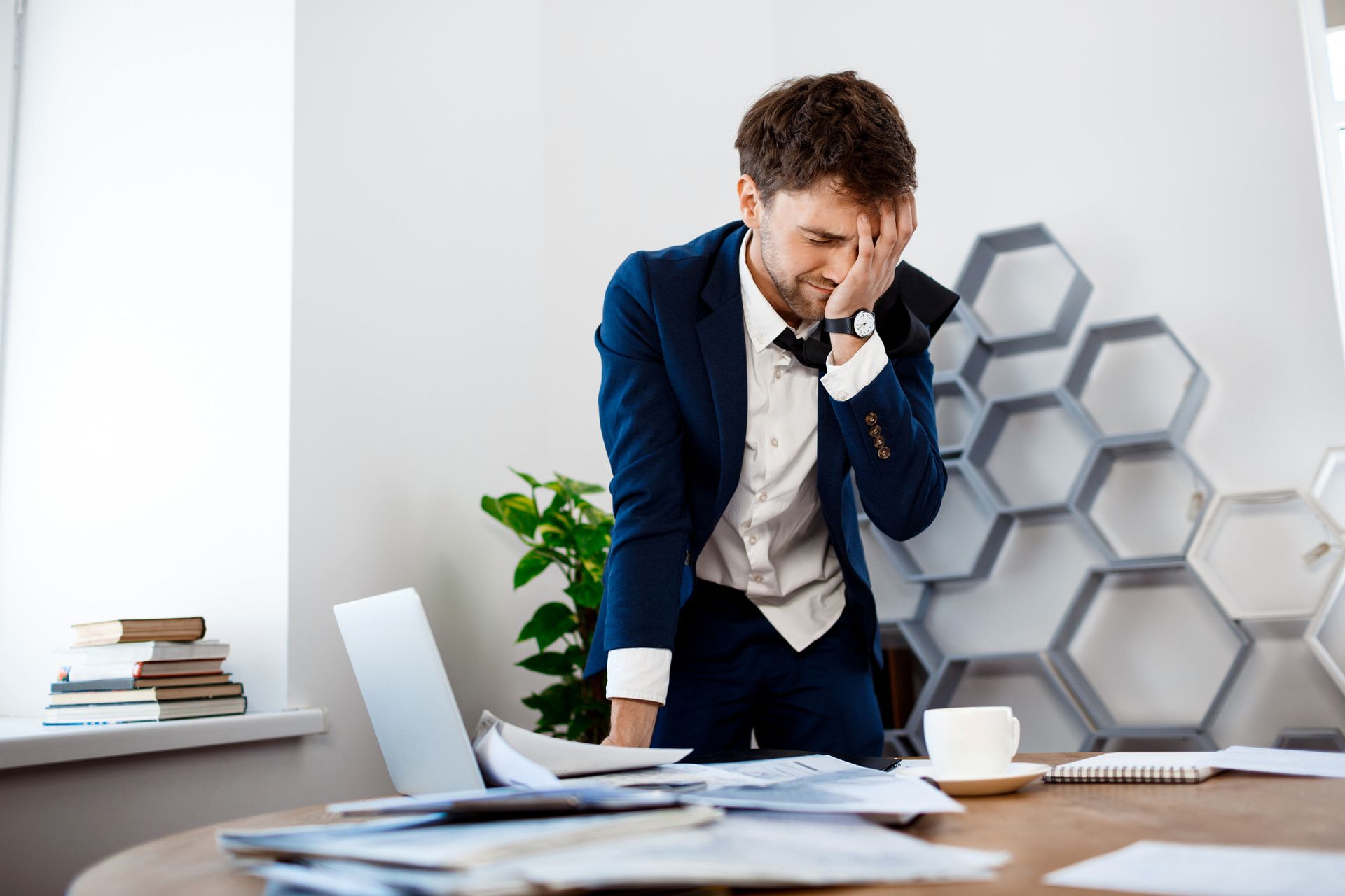 A man in a suit and tie is standing in front of a table with papers and a laptop.