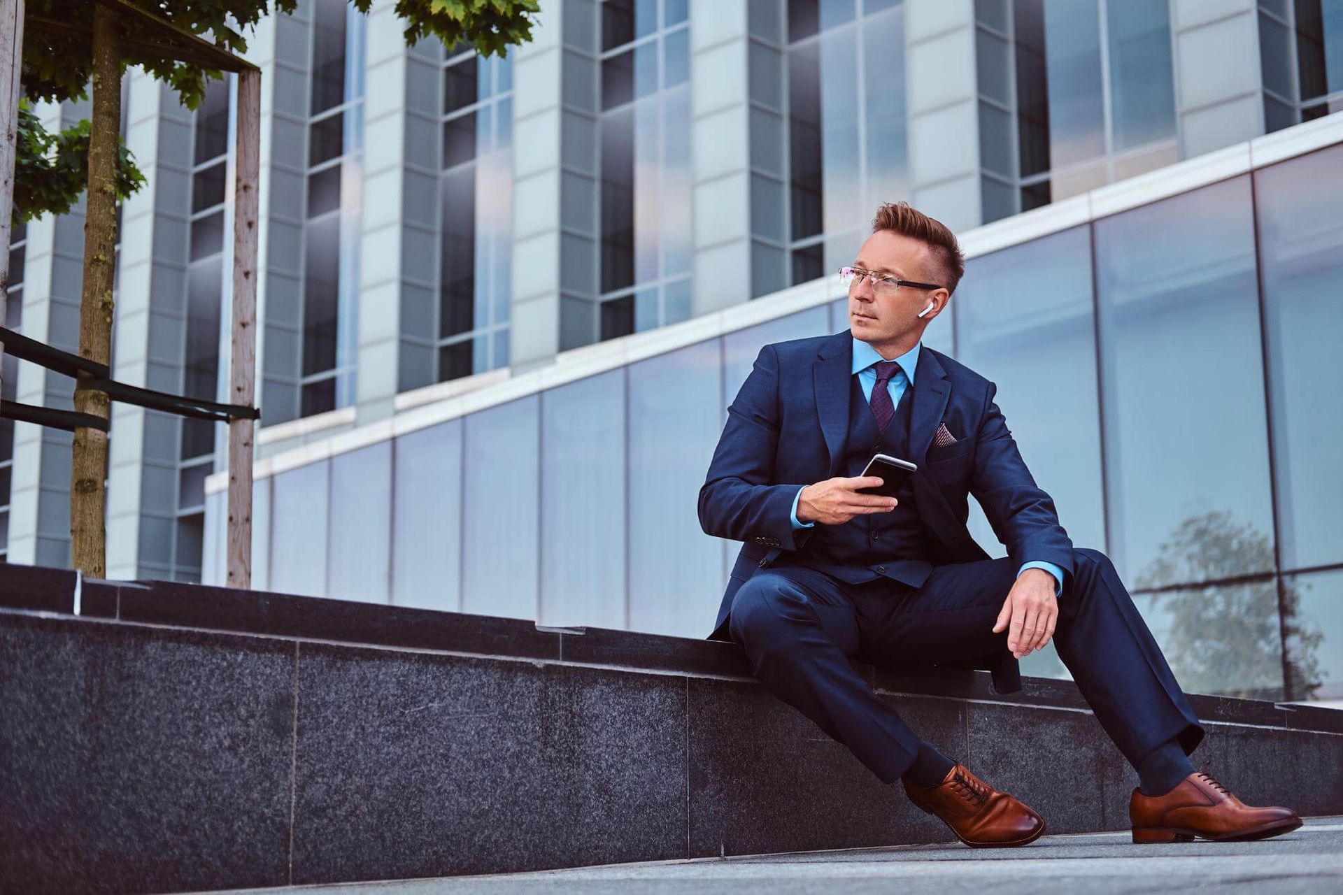 A man in a suit is sitting on a set of stairs looking at his phone.