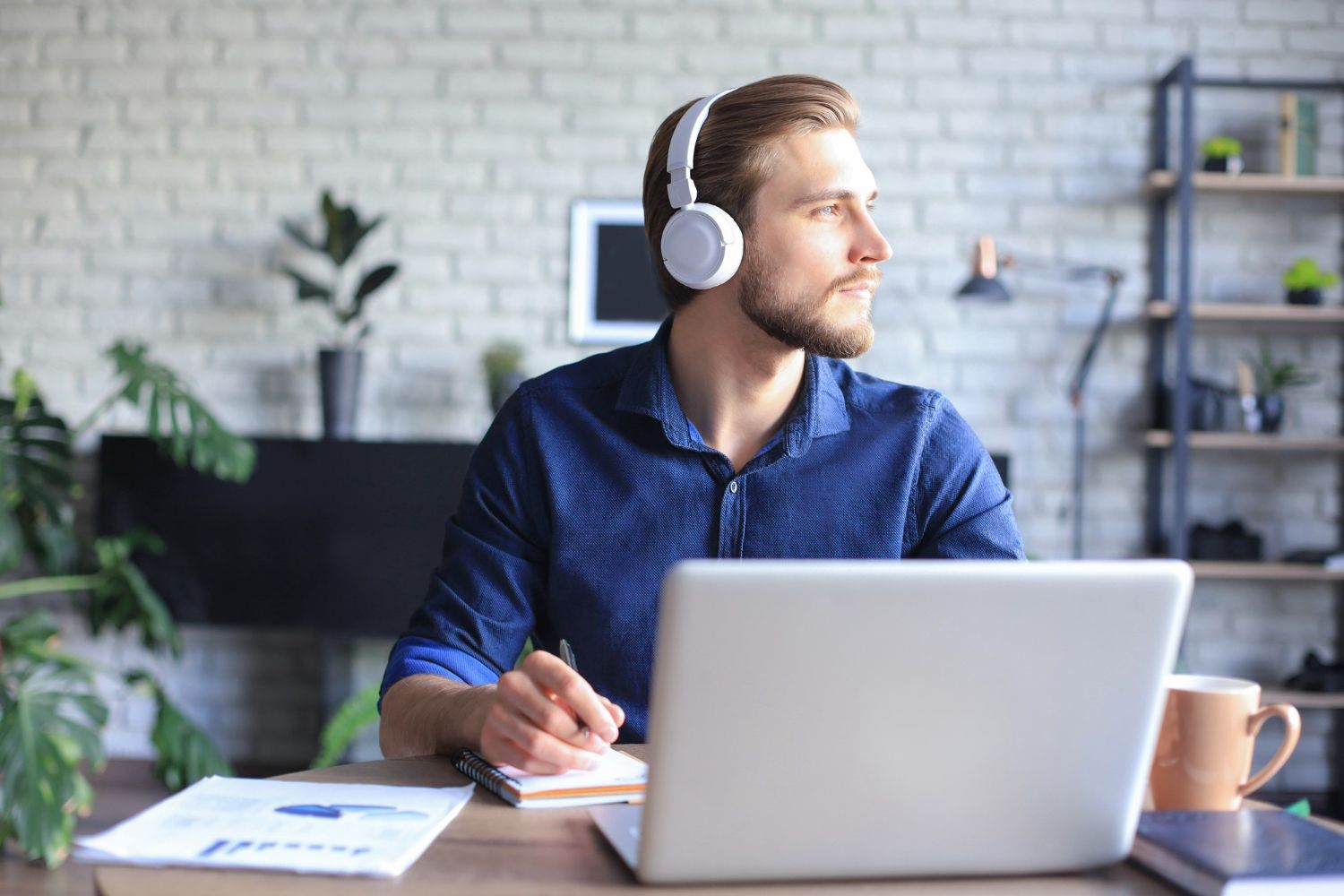 A man wearing headphones is sitting at a desk in front of a laptop computer.