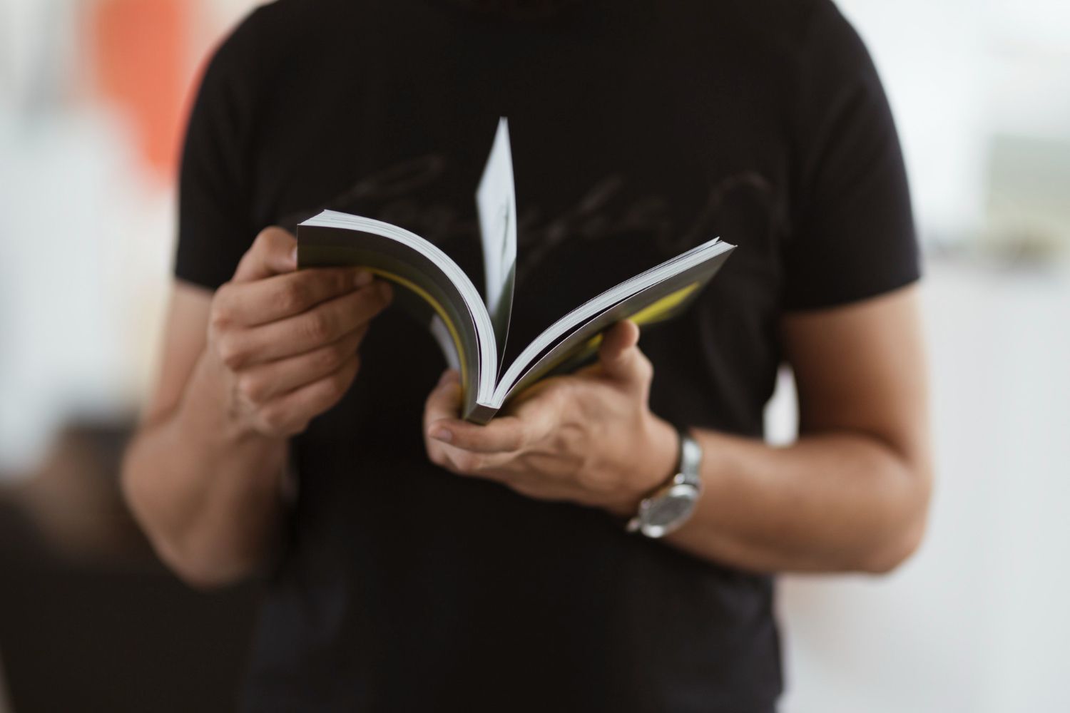 A man in a black shirt is holding an open book in his hands.