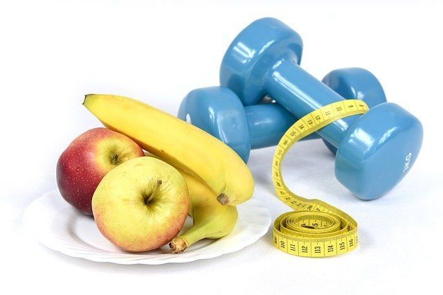 A plate of apples bananas and dumbbells next to a measuring tape