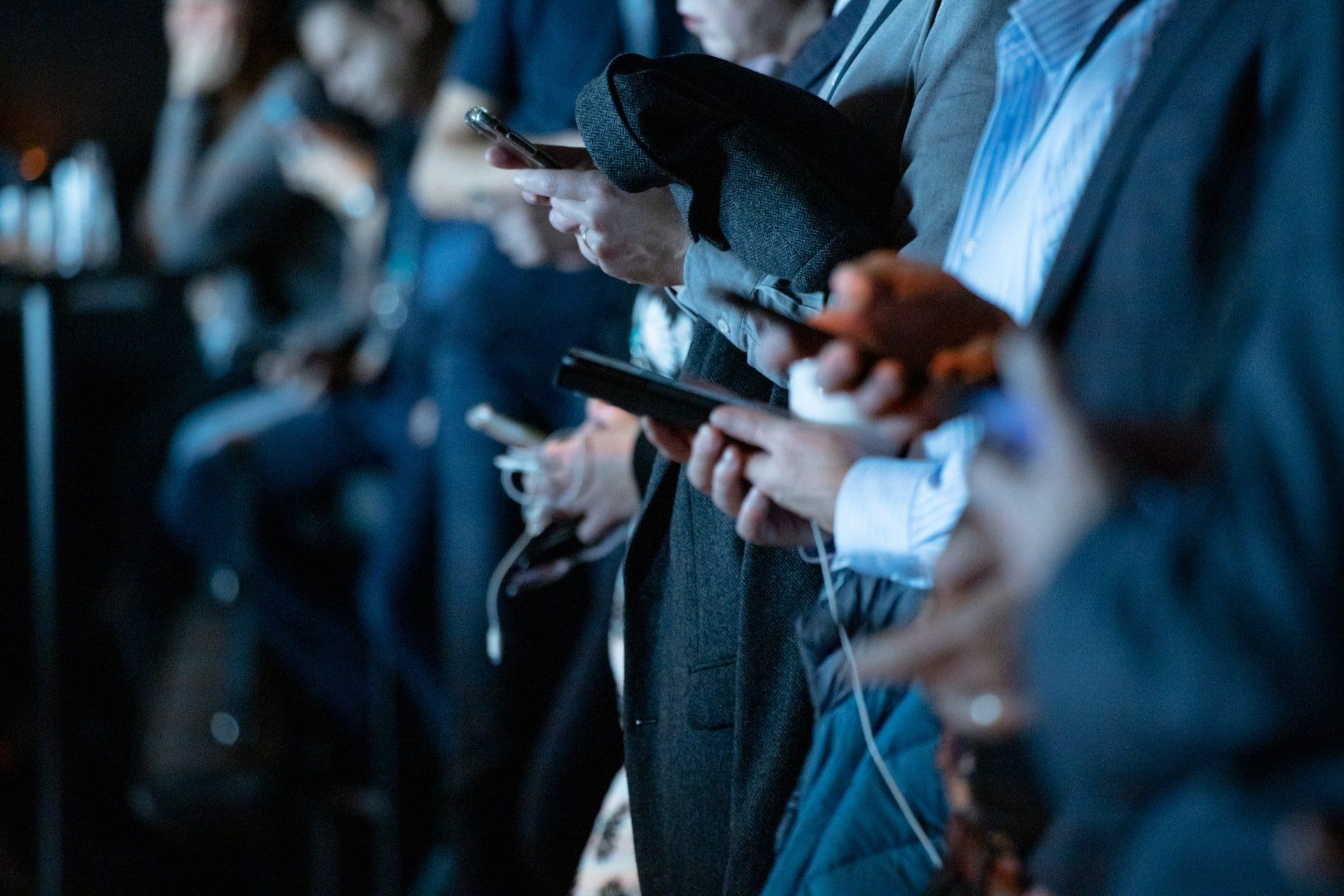 A group of people are sitting in a row looking at their phones.