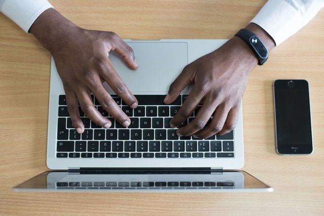 A man is typing on a laptop computer with a smart watch on his wrist.