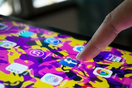 A person 's finger is pointing at a purple and yellow app on a tablet.