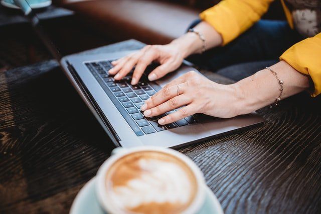 A woman is typing on a laptop next to a cup of coffee.