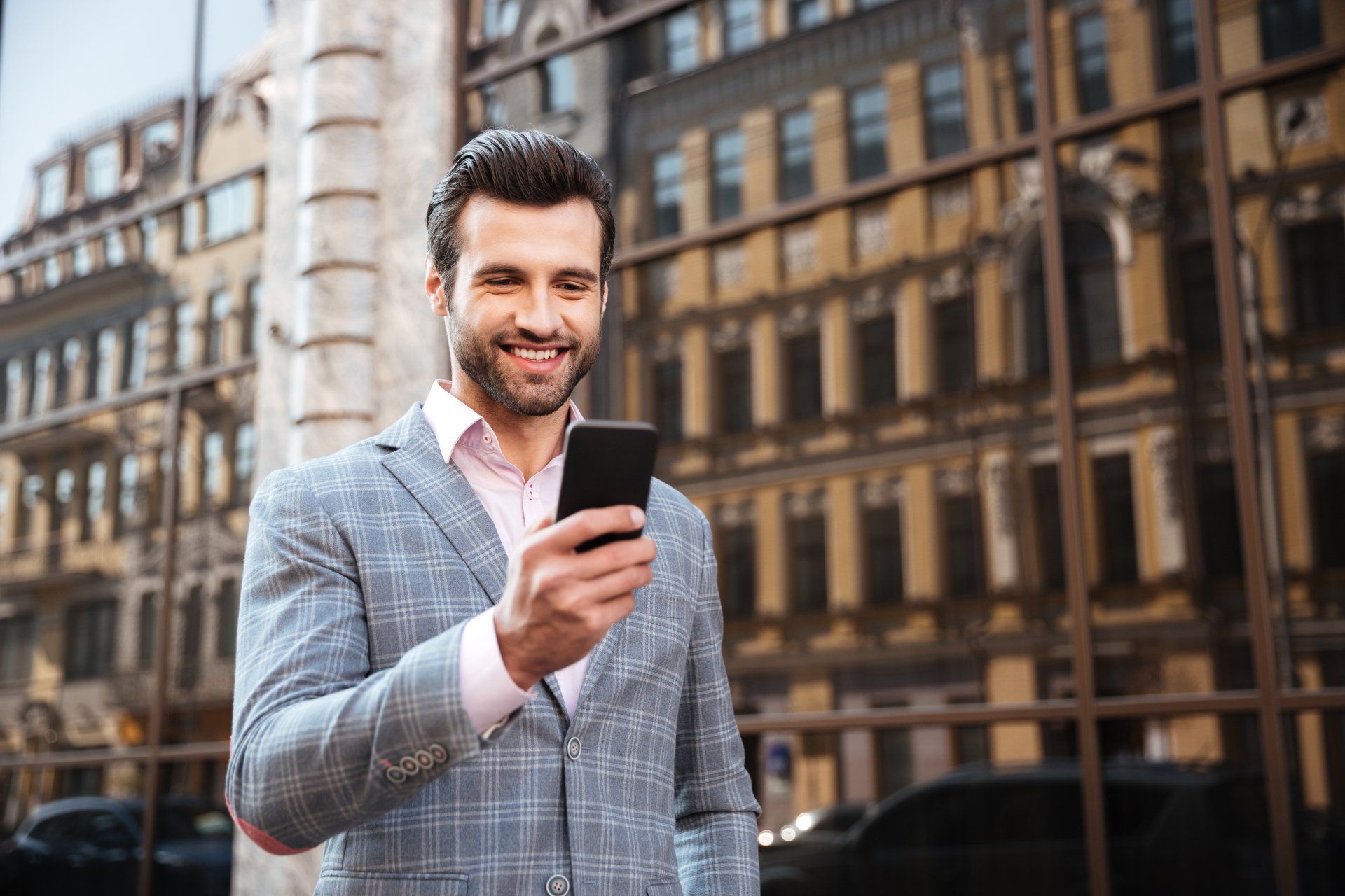 A man in a suit is holding a cell phone in front of a building.