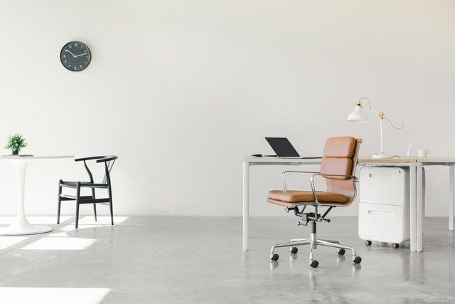 There is a clock on the wall above the desk in the office.