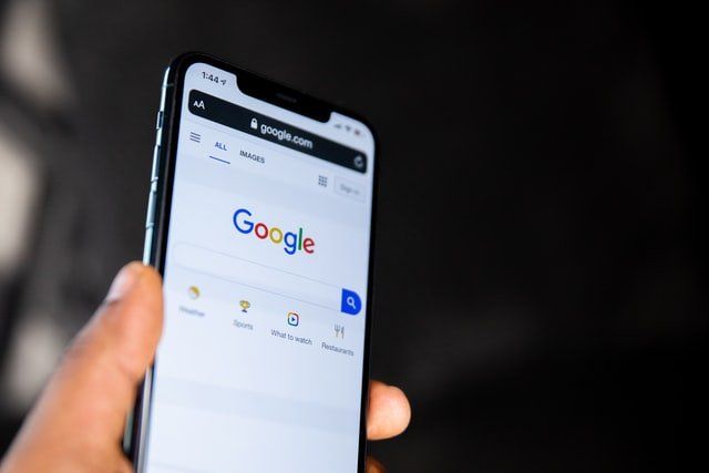 A person is holding a cell phone with the google search engine open.