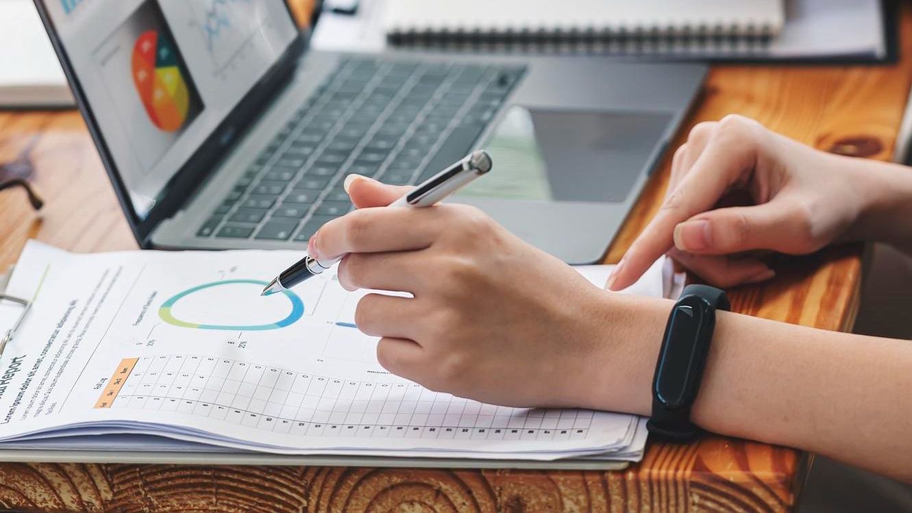 A person is writing on a piece of paper in front of a laptop computer.