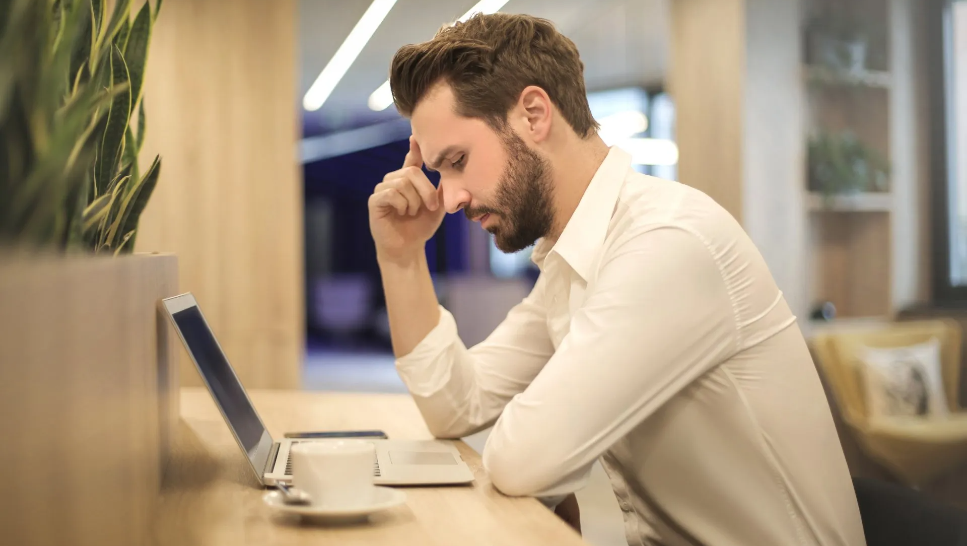 A man is sitting at a table with a laptop and a cup of coffee.