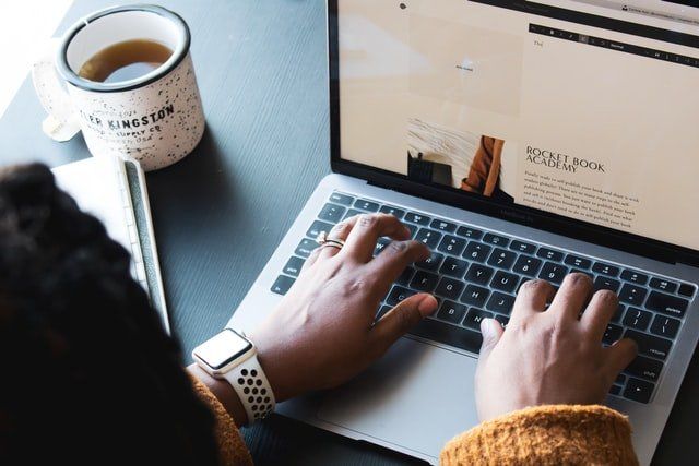 A person is typing on a laptop computer next to a cup of coffee.