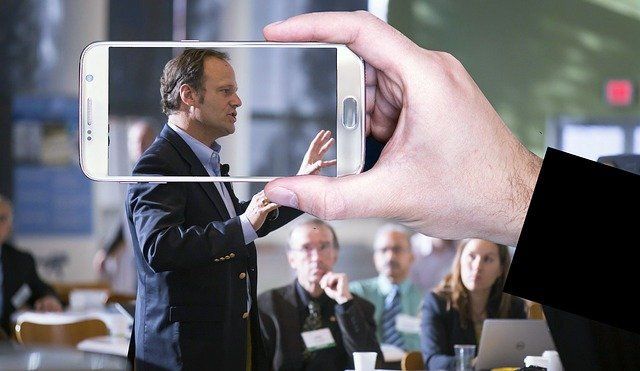 A person is taking a picture of a man giving a presentation on a cell phone.