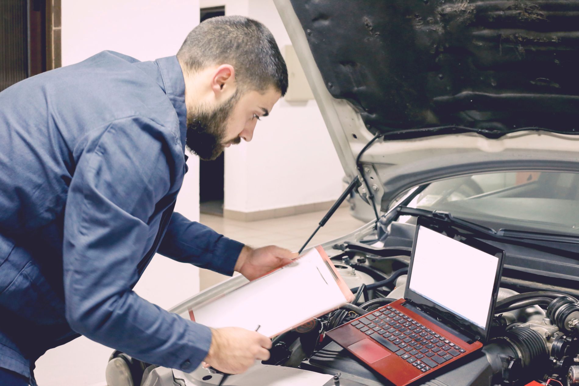 Il meccanico ispeziona il motore dell'auto con un computer portatile e un blocco per appunti.