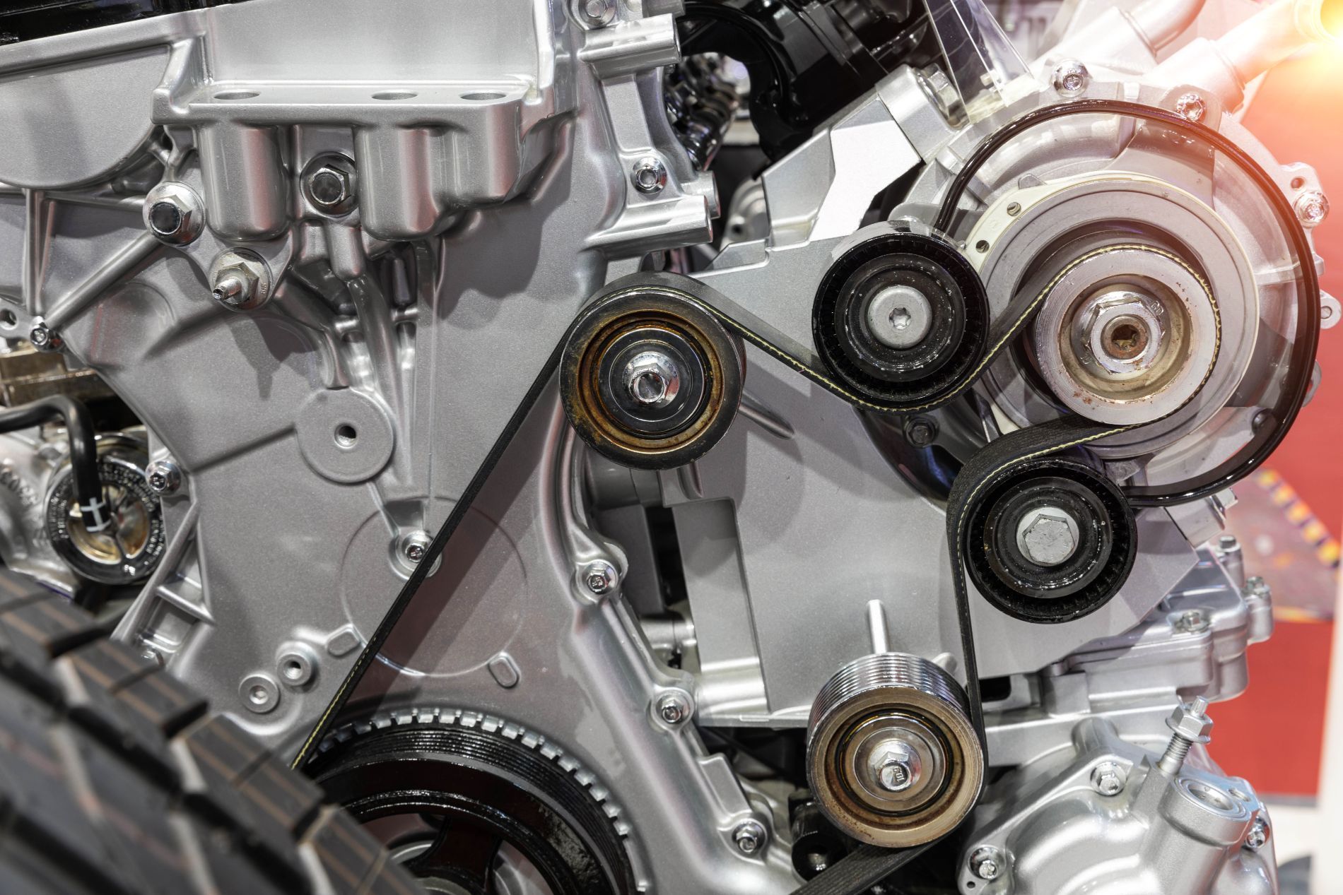 Primo piano del motore di un'auto con cinghie e pulegge in un contesto meccanico. Componenti in argento metallizzato.