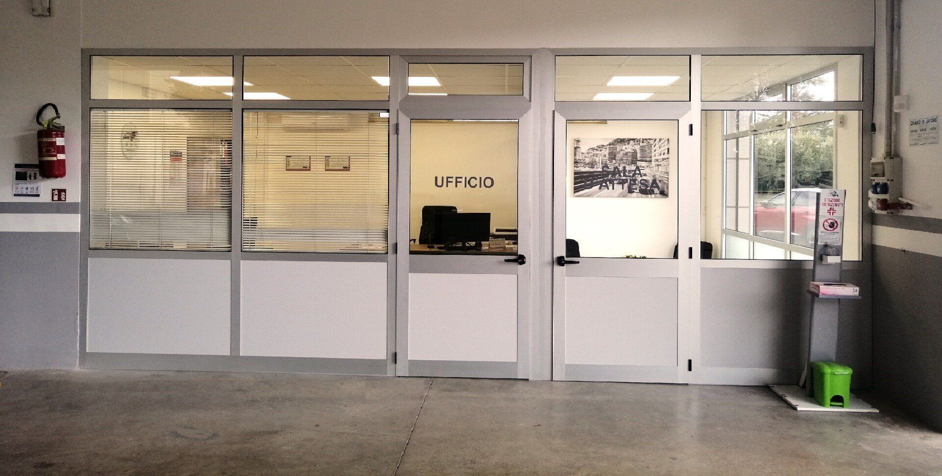 Esterno di un ufficio con finestre e porte in vetro; un estintore è montato sulla parete.