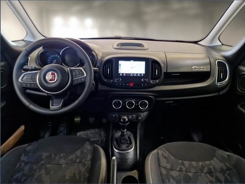 Cruscotto di una Fiat 500L, interni neri con volante, schermo dell'infotainment e cambio visibili.