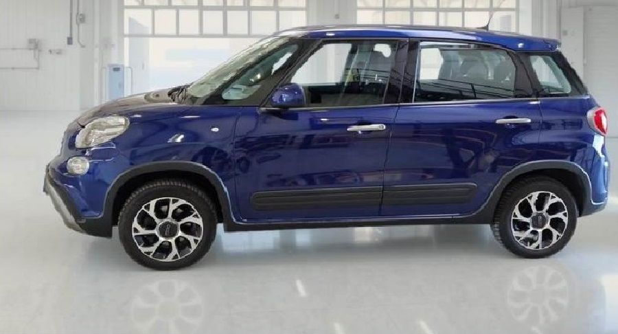 Fiat 500L blu, vista laterale, parcheggiata in uno studio con pareti bianche e ampie finestre, che mostra il design dei cerchi dell'auto.