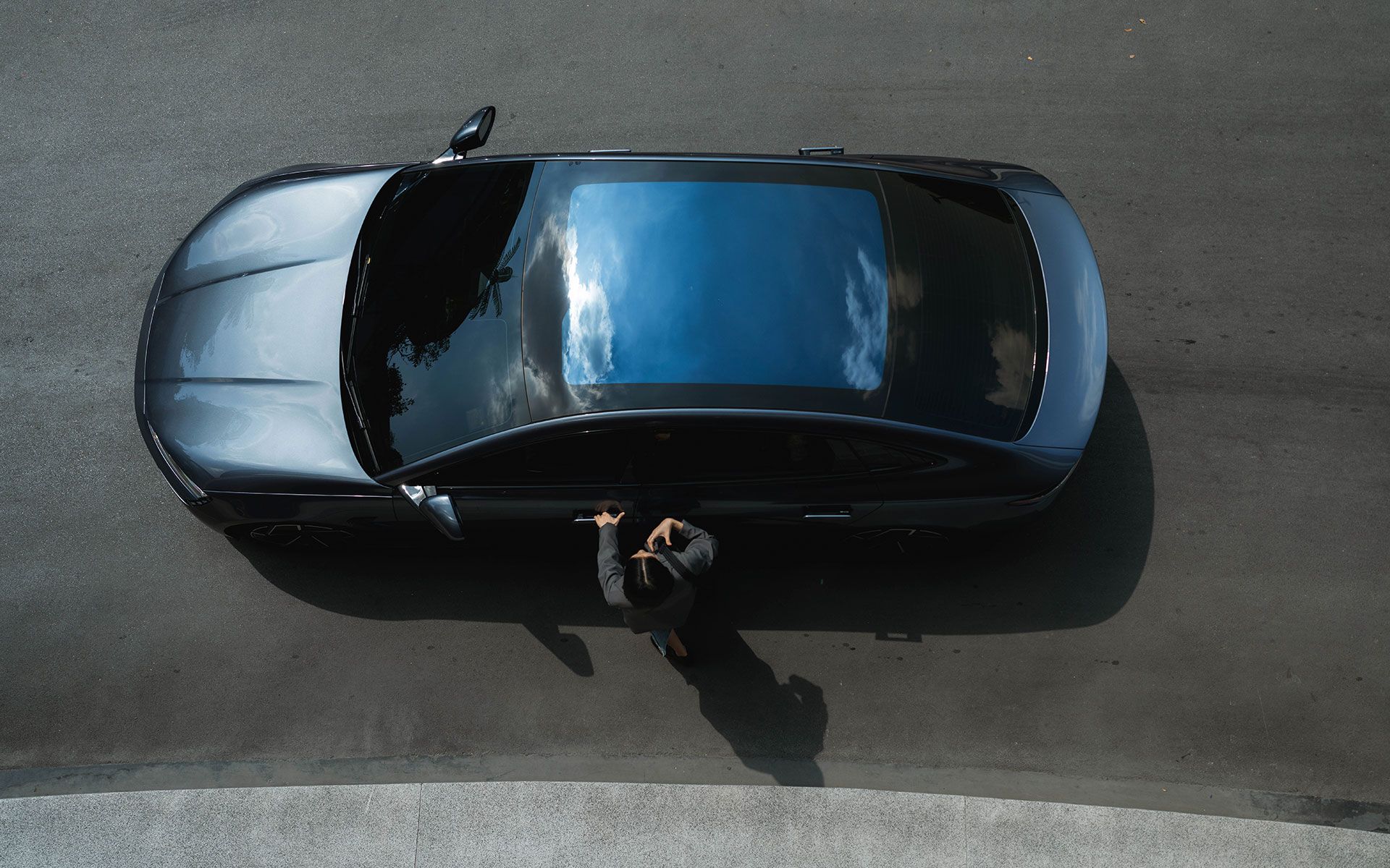 Overhead view of a black car with a person standing next to it on a paved road.