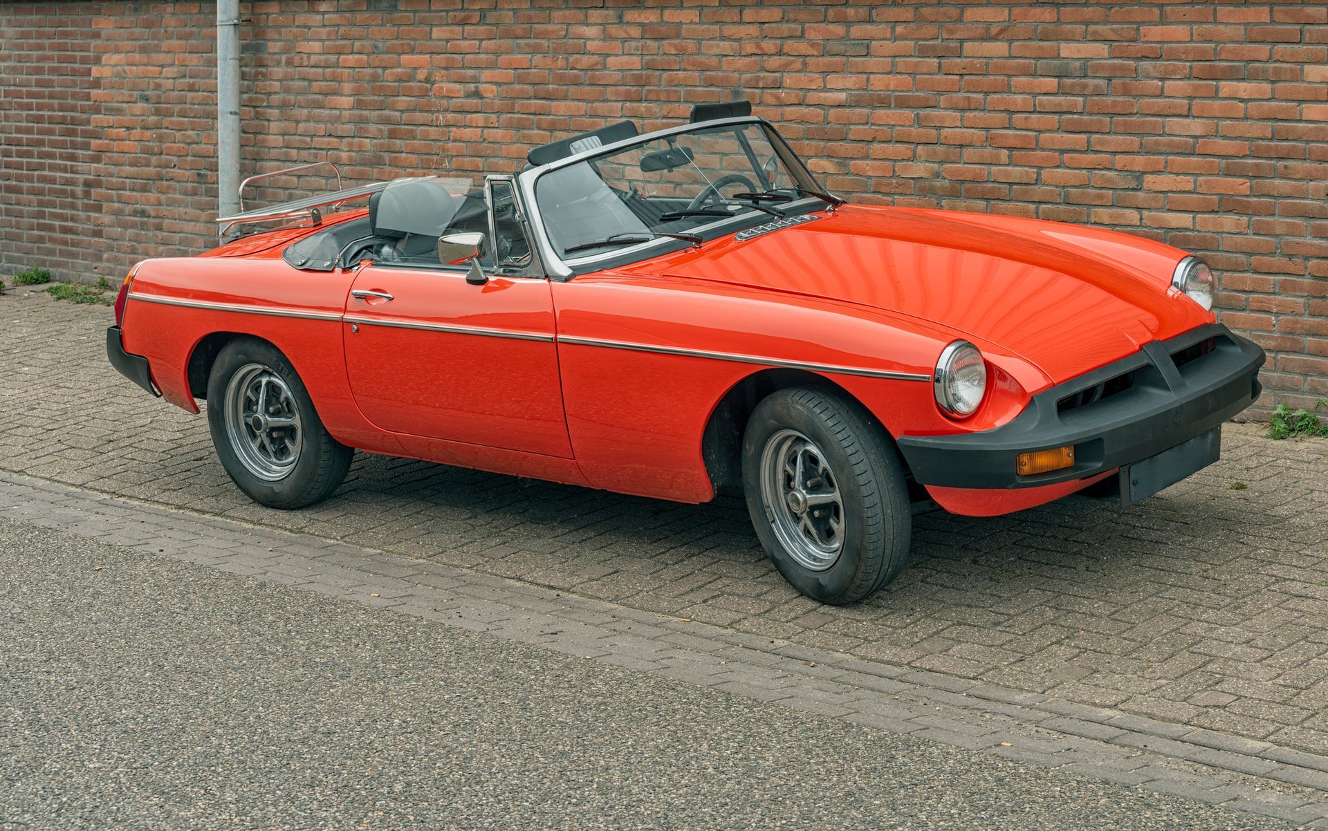 Red convertible car parked on a brick-lined street, with the top down.